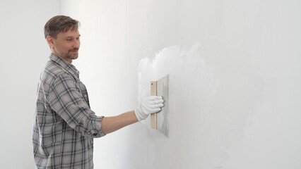 Man construction worker wearing protective gloves and plaid shirt, spreading plaster smoothly...