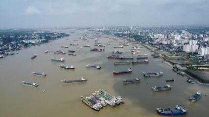 Aerial view of river with bridge, boats and buildings. Hundreds of vessels are seen anchored in Karnafuli River near Port in Chattogram, on the coastline of the Bay of Bengal. - Powered by Adobe