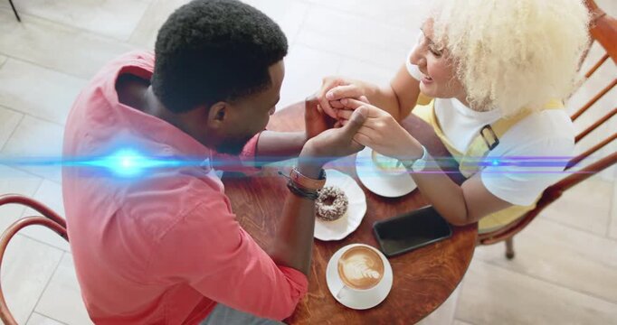AR lens-flare sweeping across café causing couple clasping hands showing love over coffee and donut - Powered by Adobe