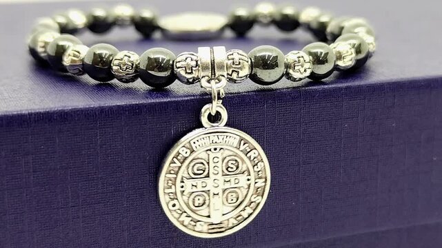 Close-up image of a Saint Benedict bracelet made of hematite beads, featuring the iconic medal gently swinging.