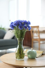 Beautiful blue cornflowers in vase and book on wooden table at home