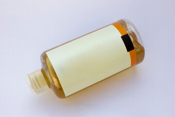 Transparent plastic bottle with amber liquid and blank label on white background. 
