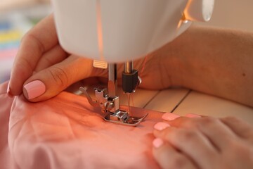 Woman working with sewing machine and fabric in workshop, closeup