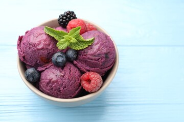 Delicious sorbet with fresh berries and mint in bowl on light blue wooden table, closeup. Space for text