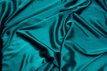 Abstract wavy green silk fabric with glossy folds, elegant background for design.