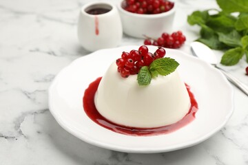 Delicious panna cotta with red currants, sauce and mint on white marble table, closeup