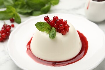 Delicious panna cotta with red currants, sauce and mint on white marble table, closeup