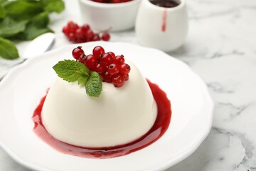 Delicious panna cotta with red currants, sauce and mint on white marble table, closeup