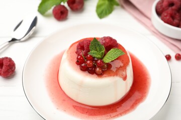 Delicious panna cotta with berries, sauce and mint on white wooden table, closeup