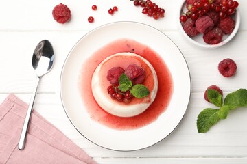 Delicious panna cotta with berries, sauce and mint on white wooden table, flat lay