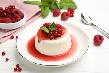 Delicious panna cotta with berries, sauce and mint on white wooden table, closeup