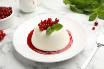 Delicious panna cotta with red currants, sauce and mint on white marble table, closeup