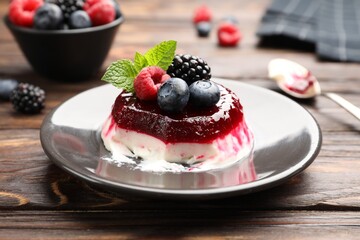 Delicious panna cotta with berries, jam and mint on wooden table, closeup