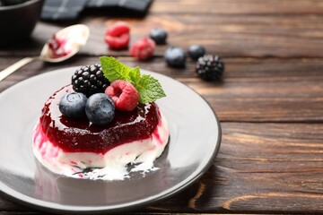Delicious panna cotta with berries, jam and mint on wooden table, closeup