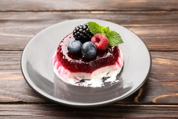Delicious panna cotta with berries, jam and mint on wooden table, closeup