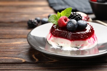 Delicious panna cotta with berries, jam and mint on wooden table, closeup
