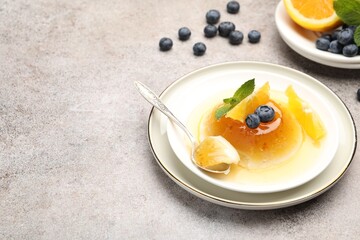 Tasty panna cotta with orange, blueberries and mint on light grey table, closeup. Space for text