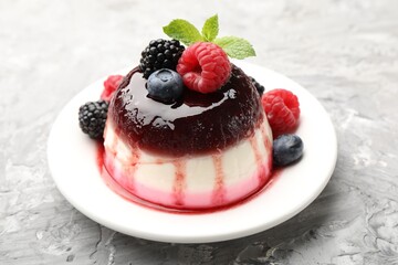 Tasty panna cotta with berries and jam on light grey table, closeup