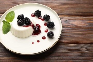 Tasty panna cotta with blackberries, mint and sauce on wooden table, closeup. Space for text