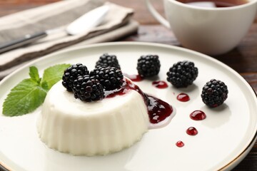 Tasty panna cotta with blackberries, mint and sauce on wooden table, closeup