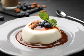 Tasty panna cotta with blueberries, almonds and sauce on black table, closeup