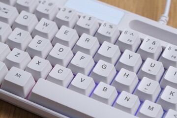 Modern white keyboard with RGB lighting on wooden table, closeup