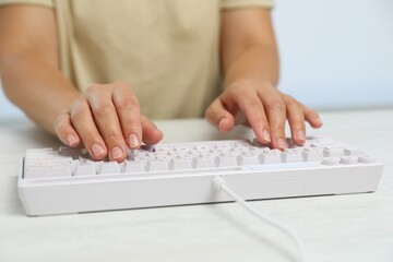 Woman typing on modern keyboard with RGB lighting at white wooden table, closeup