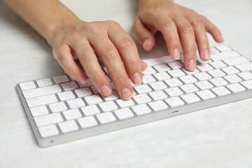 Woman typing on wireless keyboard at white wooden table, closeup