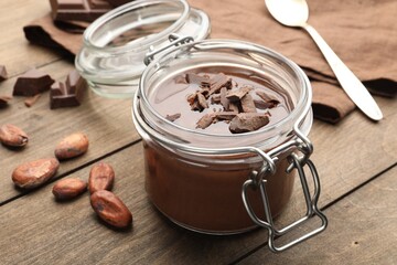 Fototapeta premium Delicious chocolate panna cotta in glass jar, nuts and spoon on wooden table, closeup