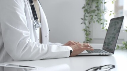 Doctor man wearing a white coat and stethoscope is typing on a laptop in a bright medical office, showcasing the intersection of healthcare and technology. Medicine and health care - Powered by Adobe