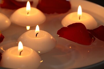Burning candles and petals in bowl of water as background, closeup