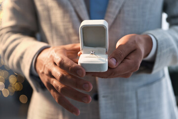 Making proposal. Man with engagement ring indoors, closeup. Bokeh effect