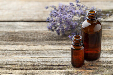 Lavender essential oil in bottles with flowers on wooden table, space for text