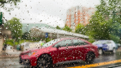 Raindrops on window with red car and buildings in background