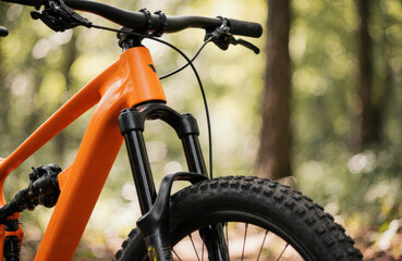 A mountain bike with an orange frame and black suspension fork in a forest setting