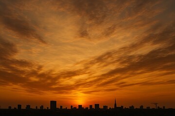 Silhouette of a city skyline against a vibrant orange and yellow sunset sky with scattered clouds
