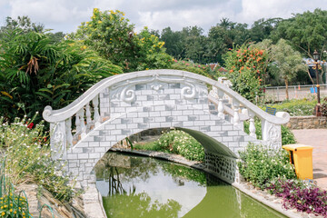 Fototapeta premium The stone bridge in the park is above the river and green plants