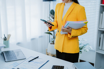 Smiling businesswoman working with financial documents, using laptop, and analyzing business data...