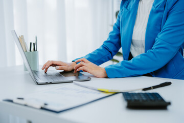 Young Asian businesswoman smiling and working on laptop computer, standing at desk in modern office, enjoying work, browsing internet, searching information, online meeting, video conference