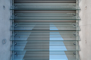 A close-up architectural detail of a modern building facade. Horizontal glass louvers are mounted on a raw concrete wall, creating a strong linear pattern.