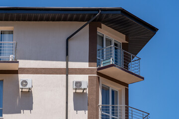 Close-up of contemporary residential building's exterior, showcasing multi-story balconies with chrome railings, large windows, and outdoor air conditioning units under vibrant blue sky