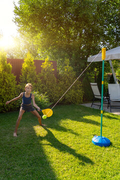 Energetic young girl plays outdoor tetherball tennis in vibrant, sunlit backyard garden, enjoying fun summer day