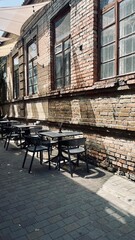 Summer cafe terrace with black tables and chairs near a brick wall