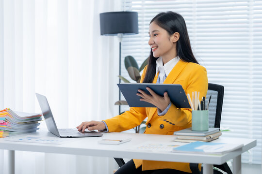 Focused at Workspace: An office portrait captures a poised woman engaged in work at her desk. She is meticulously studying documents, reflecting a dedication to work and career.