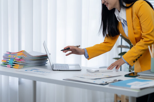 Focused Accountant Reviewing Documents: An accountant is deeply concentrated at her desk, working meticulously with a laptop and a mountain of papers in a modern office.