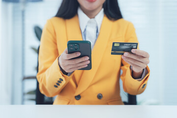 E-commerce Transaction: A professional individual in a chic, yellow blazer utilizes a smart phone and a credit card, symbolizing modern financial transactions.