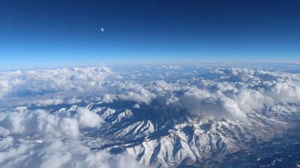 Naklejka premium Aerial view of snow-capped mountains, clouds, and a clear blue sky. Vast expanse of white clouds surrounding jagged mountain ranges. A lone moon is visible in the distant blue sky