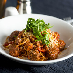 Classic Meatball Bolognese with Spaghetti, tomato sauce, Parmesan Cheese, and Arugula in bowl closeup side view of italian food