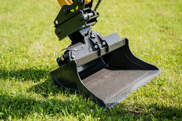 Excavator bucket resting on green grass, heavy construction equipment close-up, earthmoving machinery tool for digging and landscaping, hydraulic excavator arm detail © K
