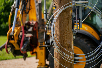Electric utility pole installation in progress with fiber optic cable spool and backhoe excavator on construction site for rural infrastructure development © K